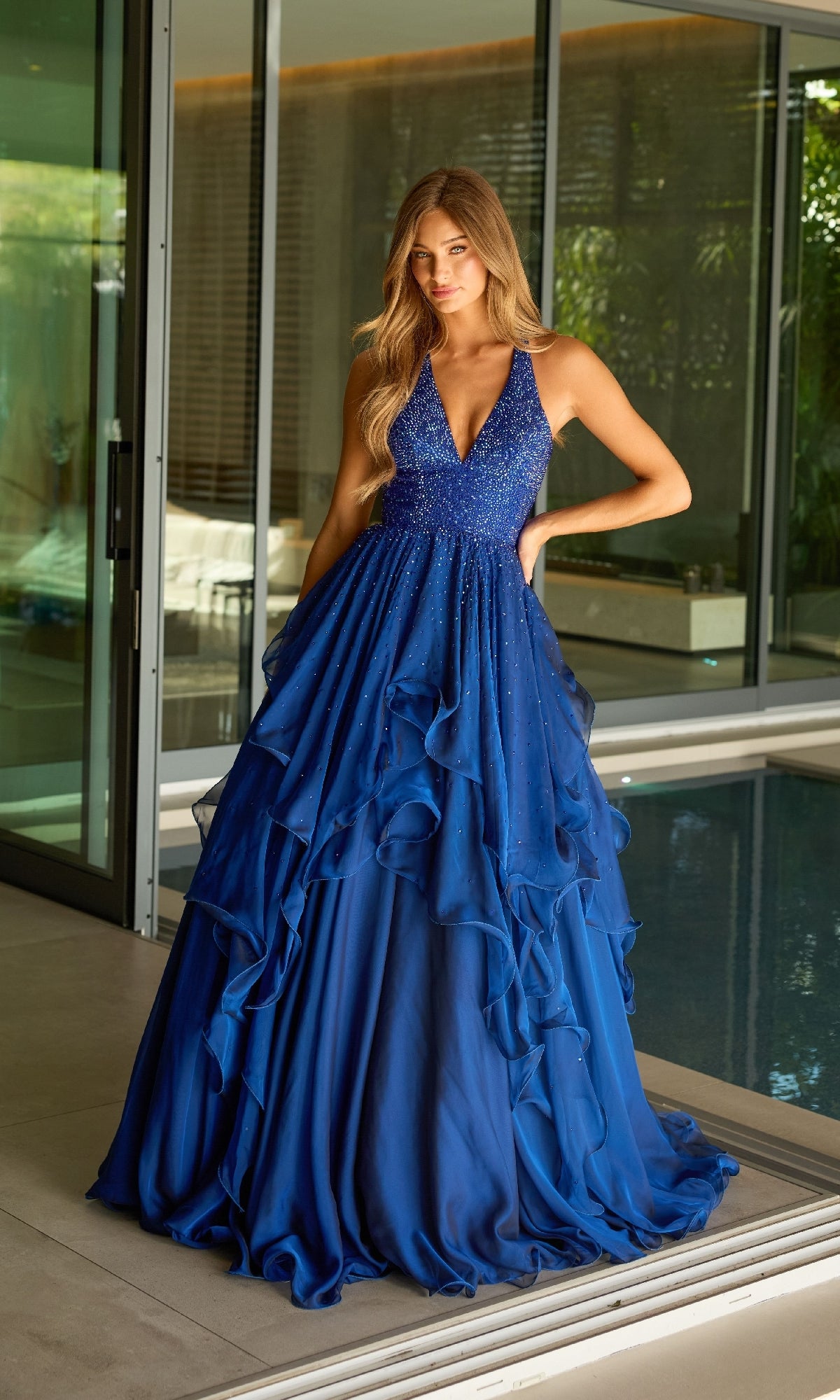 Indoors by a pool, a woman wears the Ava Presley 42235: a long halter A-line formal dress.